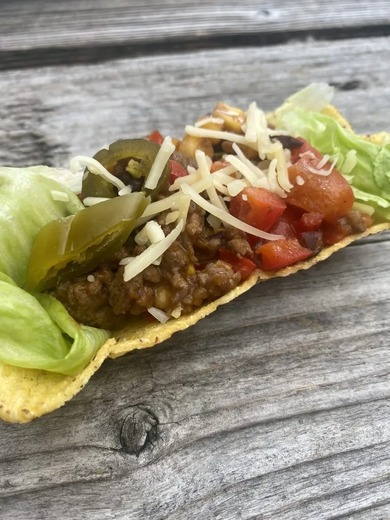 Taco met gehakt, jalapeño en geraspte kaas op een houten tafel